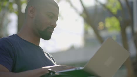 Unteransicht-Eines-Jungen-Afroamerikanischen-Mannes-Im-Park,-Der-Am-Laptop-Arbeitet